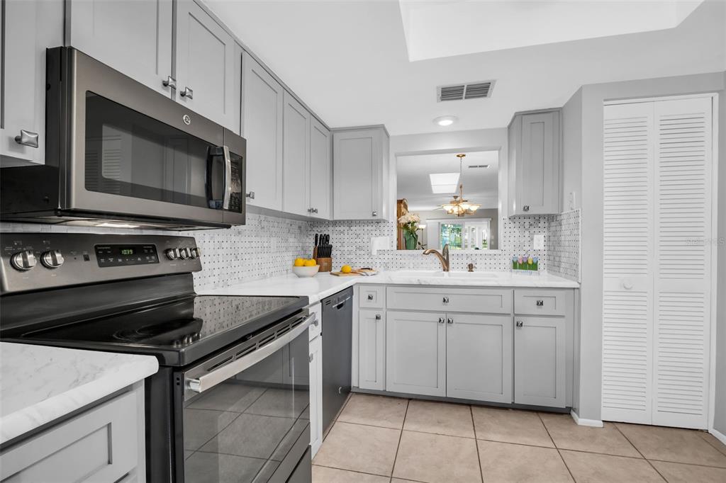 A kitchen featuring gray cabinets, stainless steel appliances, white countertops, and a tiled backsplash — 860 MACLAREN DRIVE N UNIT B, PALM HARBOR, FL