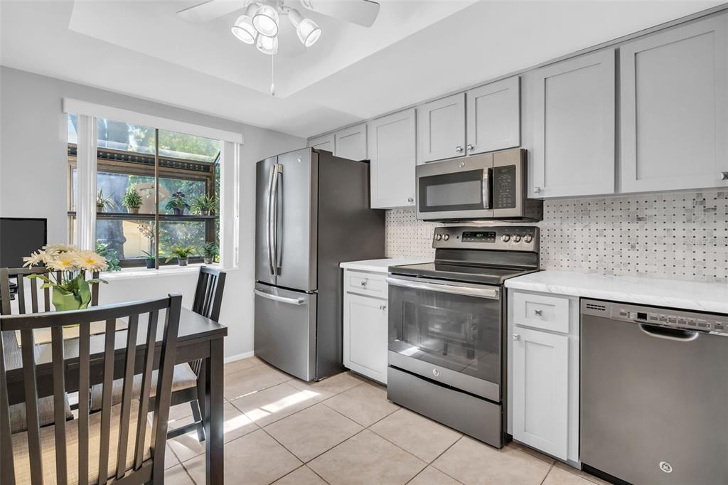 A kitchen with light gray cabinets, stainless steel appliances, and a dining area by a window — 860 MACLAREN DRIVE N UNIT B, PALM HARBOR, FL