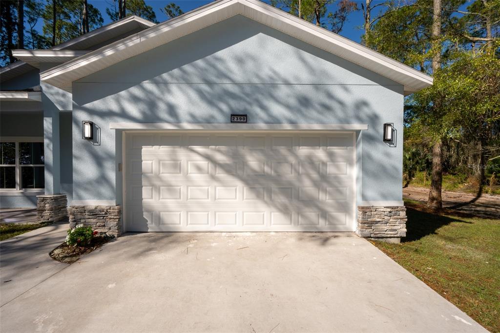 A light blue house exterior features a two-car garage, stone accents, and a concrete driveway — 2390 9TH AVE, DELAND, FL