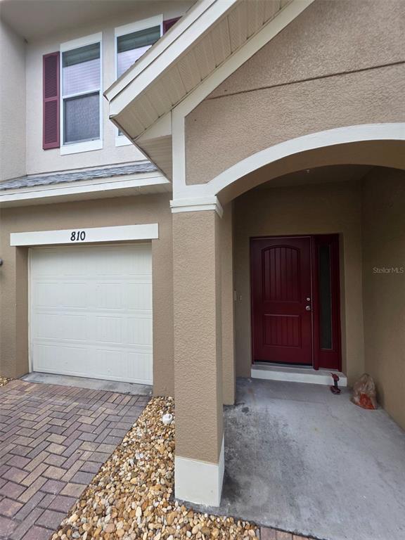 The exterior of a house features a tan stucco facade, a red front door, and a garage — 810 CALLISTA CAY LOOP, TARPON SPRINGS, FL