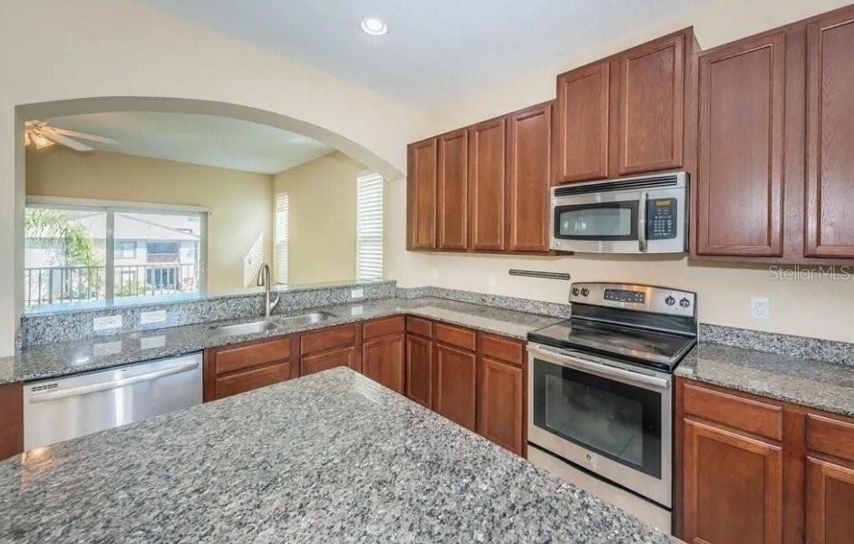 A kitchen with wood cabinets, granite countertops, stainless steel appliances, and an arched wall opening — 810 CALLISTA CAY LOOP, TARPON SPRINGS, FL