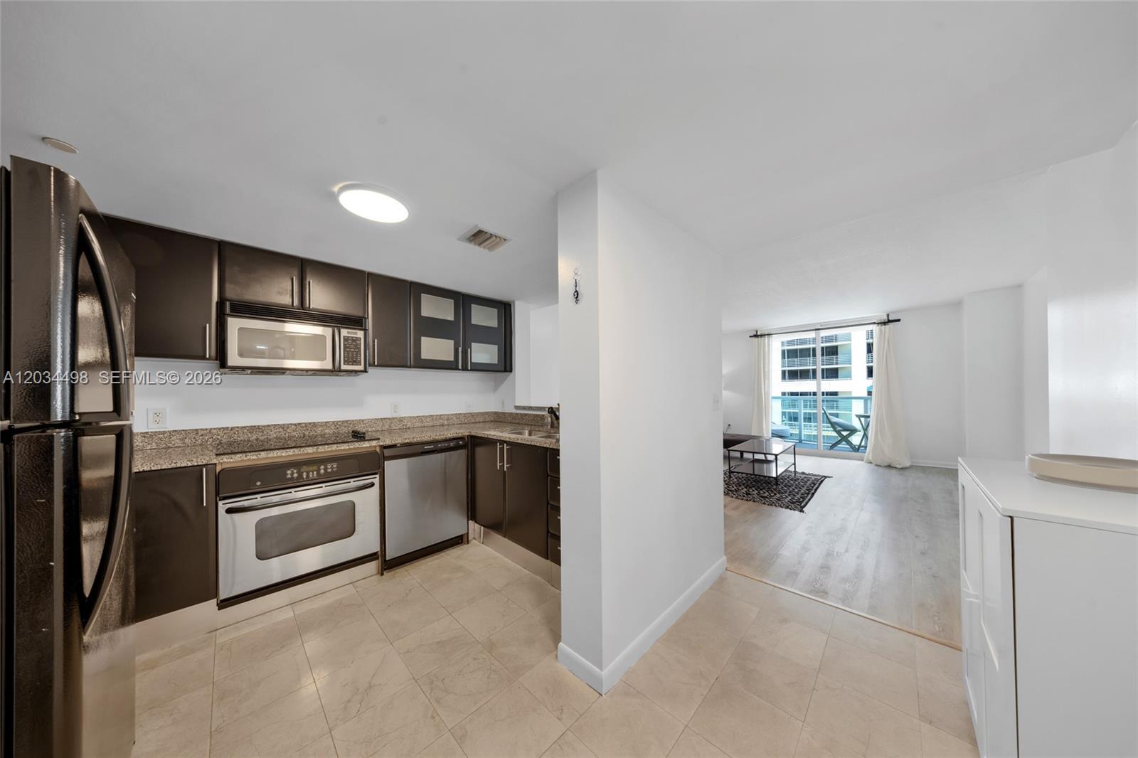A kitchen with dark cabinets and stainless steel appliances opens into a living area — 2101 Brickell Ave # 605, Miami FL 33129, MIAMI, FL