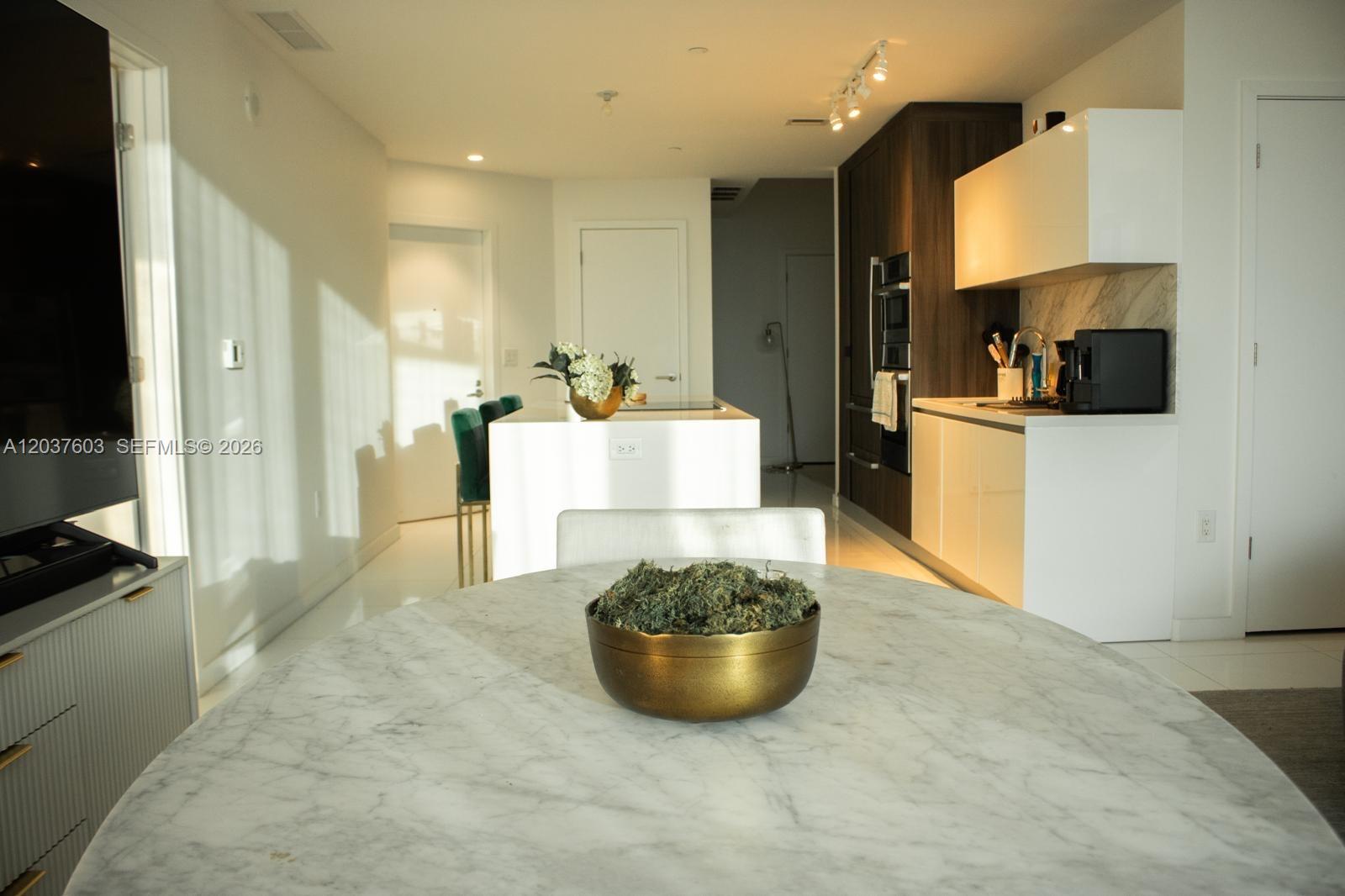 A modern kitchen and dining area feature a marble table, white cabinetry, and dark wood accents — 851 NE 1st Ave # 4806, Miami FL 33132, MIAMI, FL