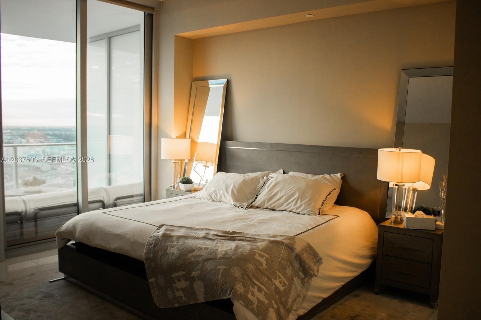 A bedroom features a bed with a patterned throw, two lamps, and floor-to-ceiling windows — 851 NE 1st Ave # 4806, Miami FL 33132, MIAMI, FL