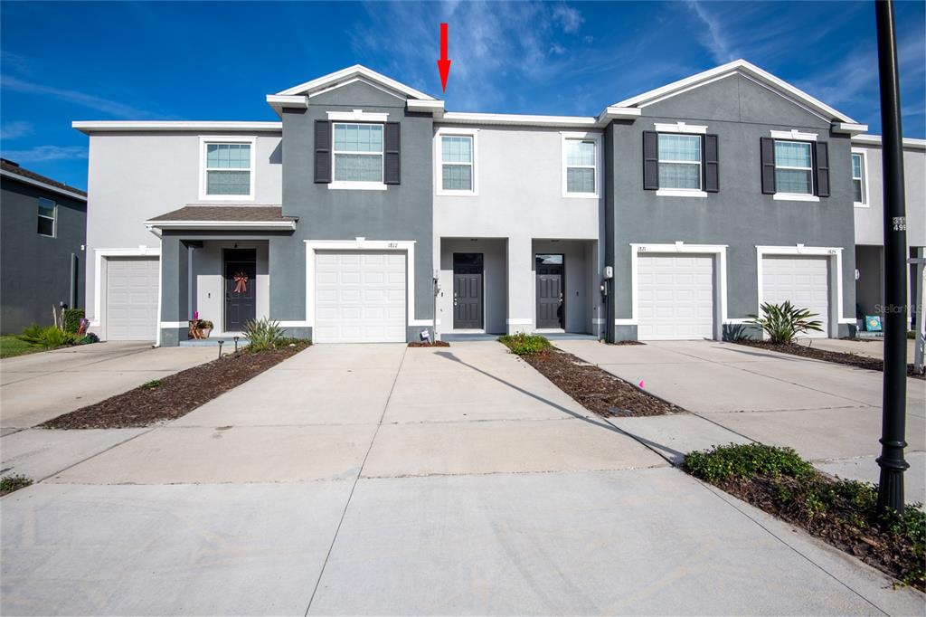 A row of two-story townhouses with gray and white stucco facades and attached garages — 1817 HOVENWEEP ROAD, WESLEY CHAPEL, FL