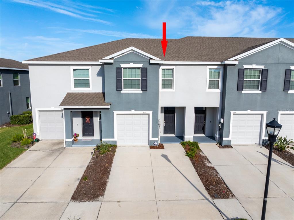 A red arrow points to the roofline of a two-story townhouse with a gray exterior — 1817 HOVENWEEP ROAD, WESLEY CHAPEL, FL