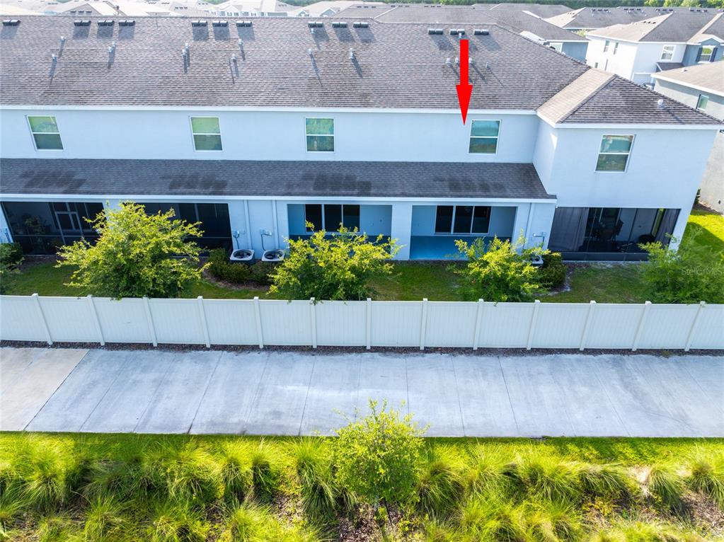 An exterior view of the rear of a multi-story townhouse with a white fence — 1817 HOVENWEEP ROAD, WESLEY CHAPEL, FL