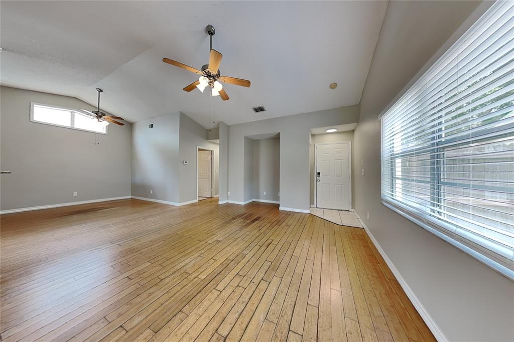 An empty living room features hardwood floors, vaulted ceilings with two fans, and a door — 13344 LARAWAY DRIVE, RIVERVIEW, FL