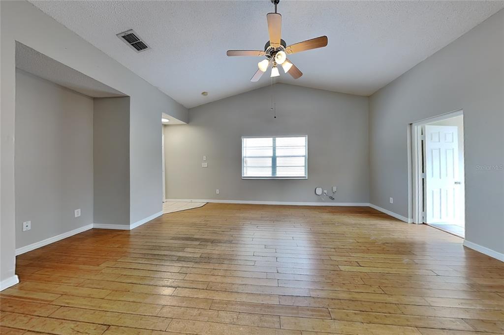 An empty living room features light gray walls, a vaulted ceiling, and wood-look flooring — 13344 LARAWAY DRIVE, RIVERVIEW, FL