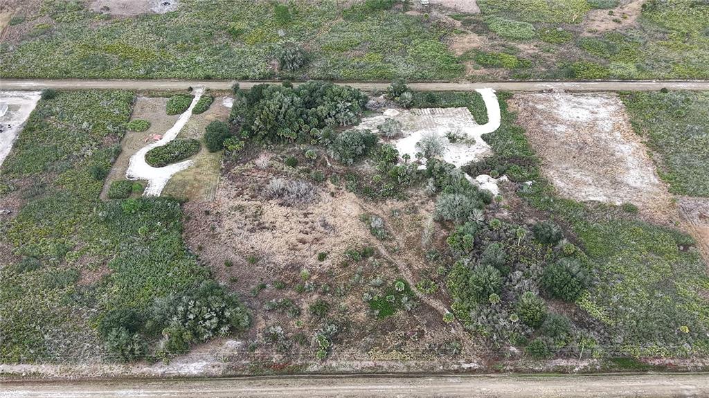 An aerial view shows a vacant, partially cleared lot with vegetation and dirt paths — 21867 NW 276TH STREET, OKEECHOBEE, FL
