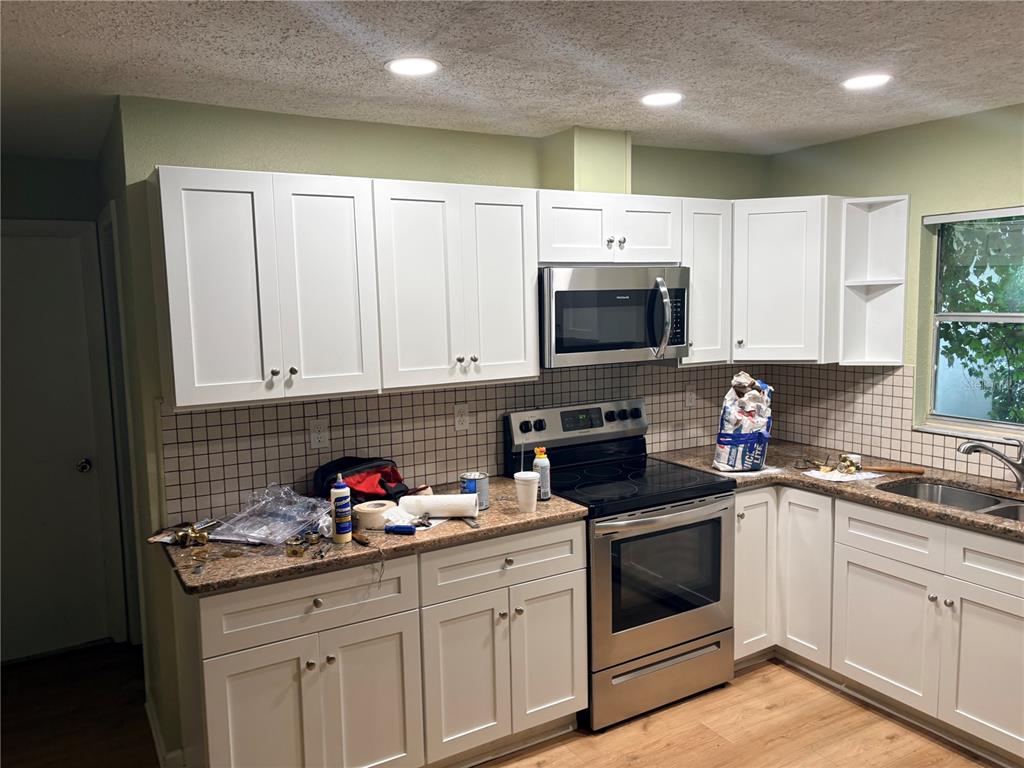 A kitchen features white shaker cabinets, stainless steel appliances, granite countertops, and a tiled backsplash — 9080 GENEVA STREET, SPRING HILL, FL