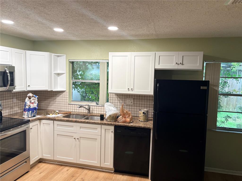 A kitchen features white cabinets, granite countertops, a black refrigerator, and a tiled backsplash — 9080 GENEVA STREET, SPRING HILL, FL