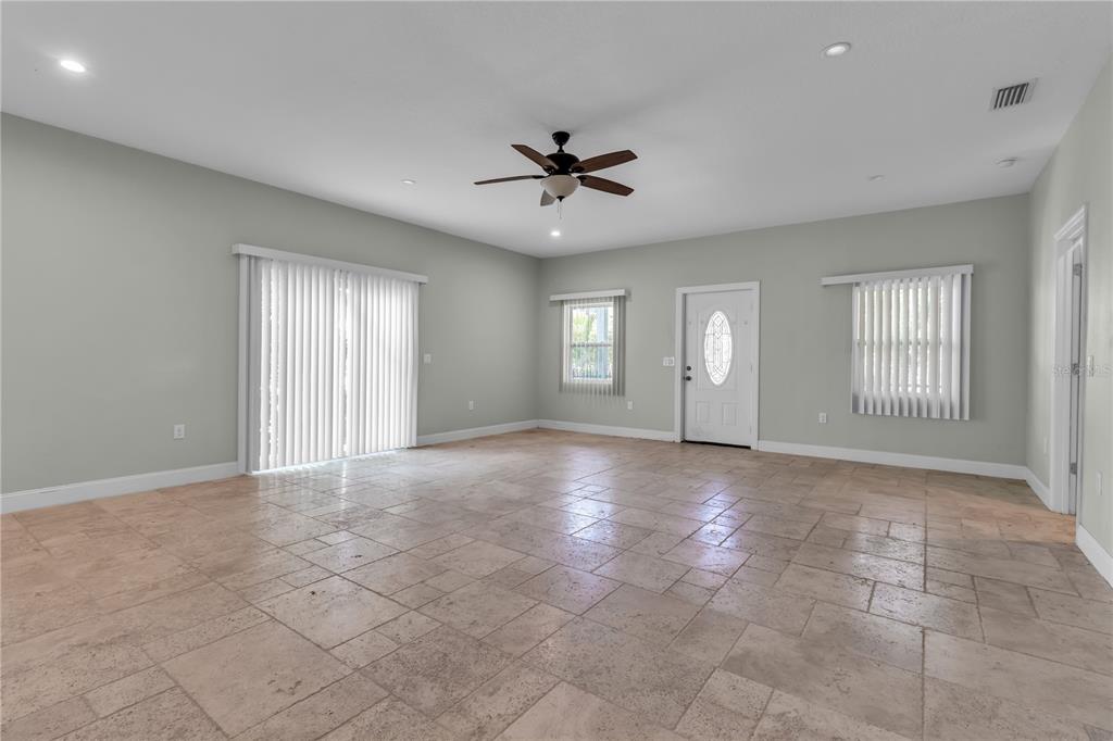An empty living room features light-colored tile flooring, a ceiling fan, and a sliding door — 1536 25TH STREET, SARASOTA, FL