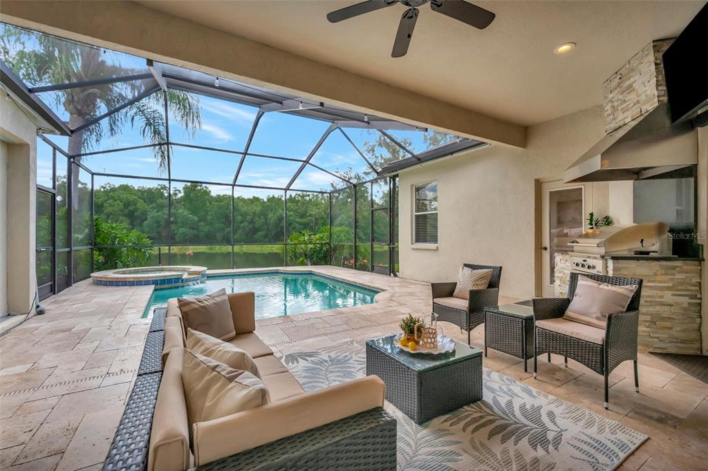 A covered patio features a pool, hot tub, outdoor kitchen, and seating area overlooking water — 8523 PORTAGE AVENUE, TAMPA, FL