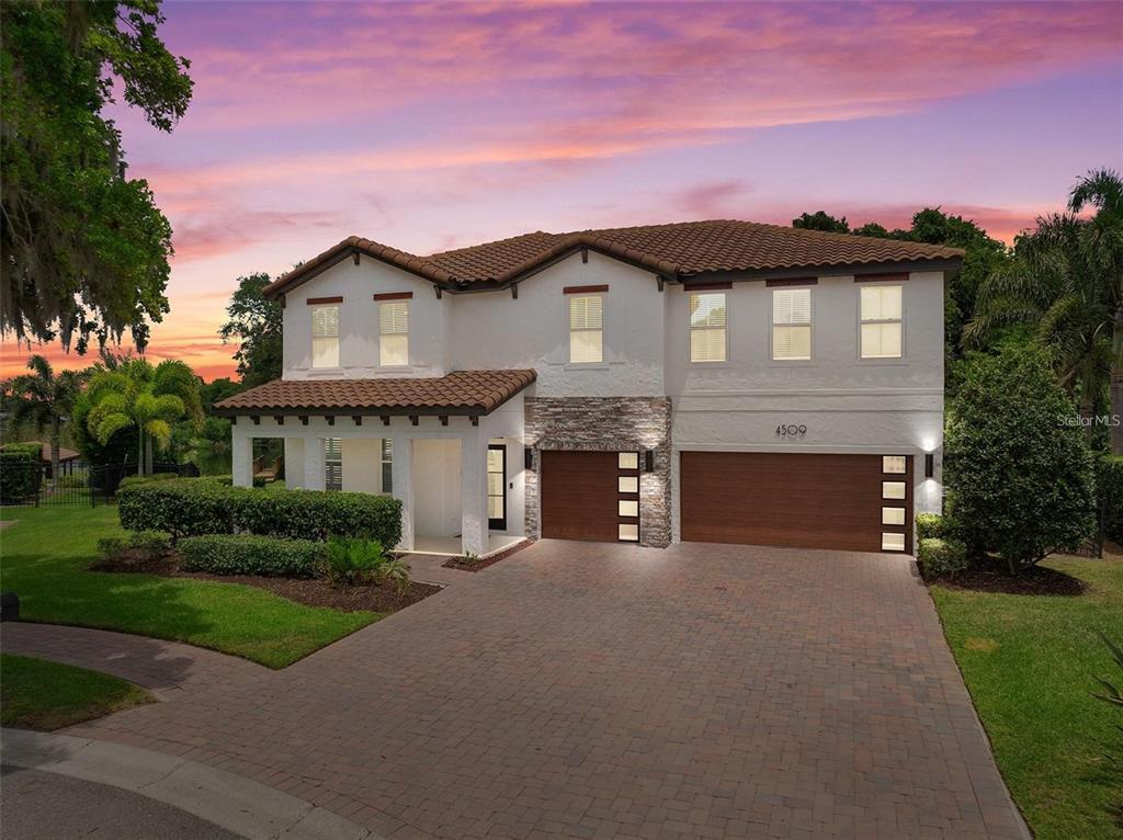 A two-story house with a tile roof, stone accents, and a paved driveway at sunset — 4509 PATRICIA ANN COURT, ORLANDO, FL