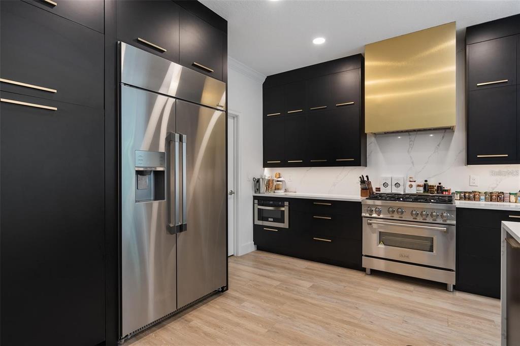 A modern kitchen features black cabinetry, stainless steel appliances, and a prominent gold range hood — 4509 PATRICIA ANN COURT, ORLANDO, FL