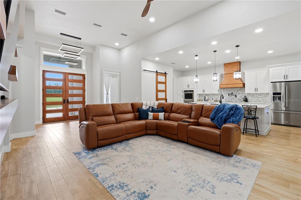 A spacious open-concept living area features a brown leather sectional, light wood floors, and kitchen — 18711 NW 138TH AVENUE, ALACHUA, FL