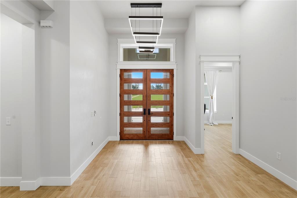 A bright entryway features light wood flooring, white walls, and double wooden front doors — 18711 NW 138TH AVENUE, ALACHUA, FL