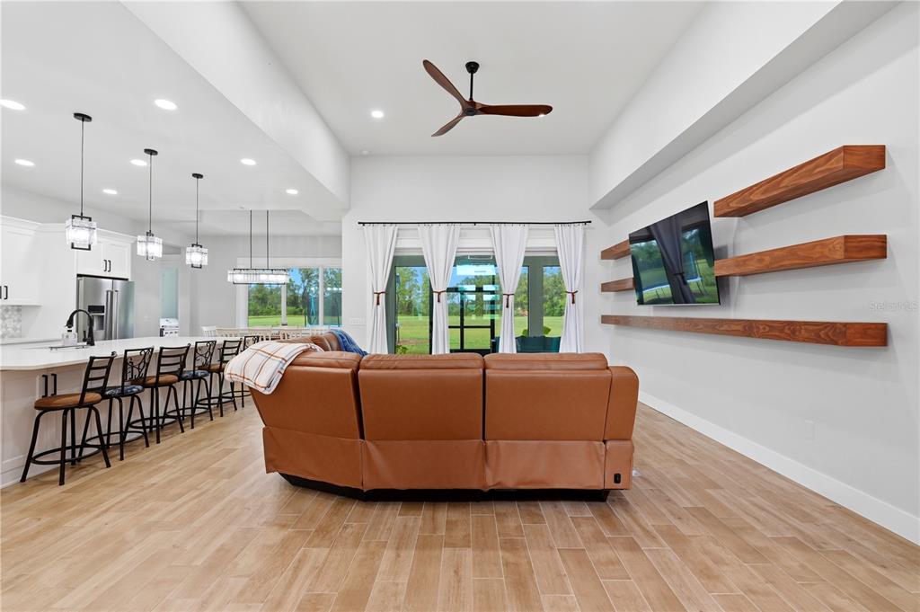 A living room with a brown leather sectional, wood floating shelves, and an open kitchen — 18711 NW 138TH AVENUE, ALACHUA, FL