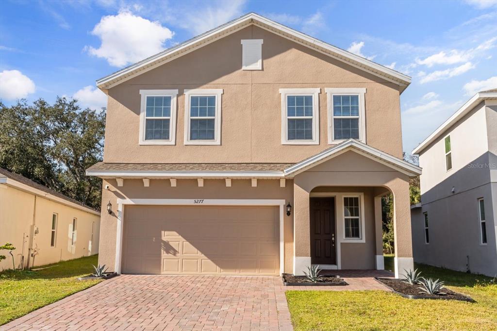A two-story suburban house with a tan stucco exterior, a two-car garage, and a driveway — 5277 ROYAL POINT AVENUE, KISSIMMEE, FL