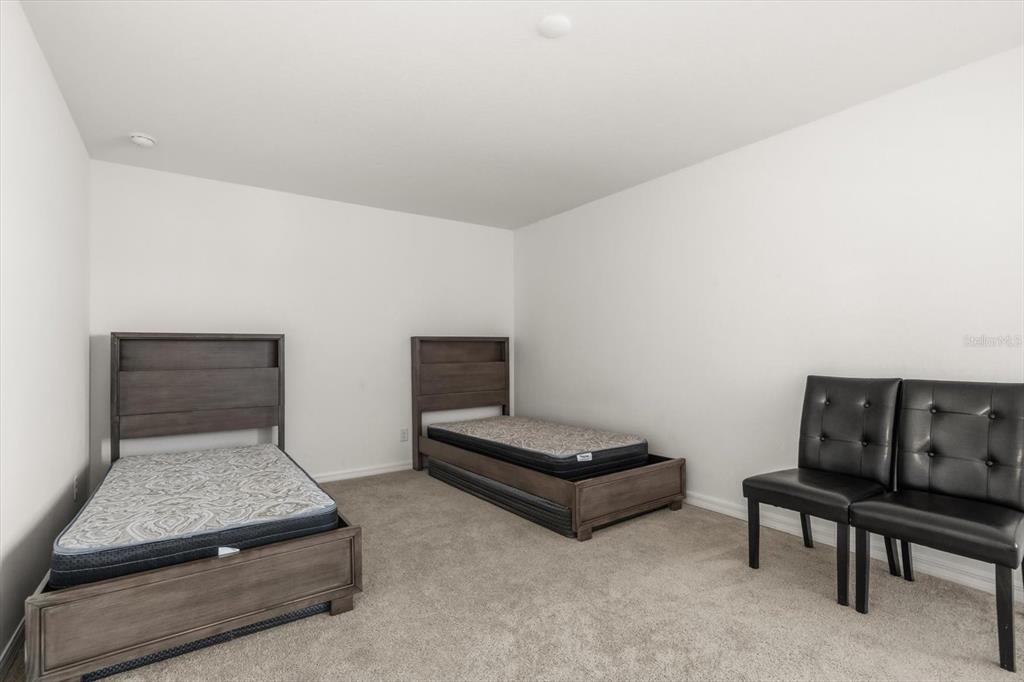 A bedroom features two wooden twin beds and two black tufted chairs on carpet — 5277 ROYAL POINT AVENUE, KISSIMMEE, FL