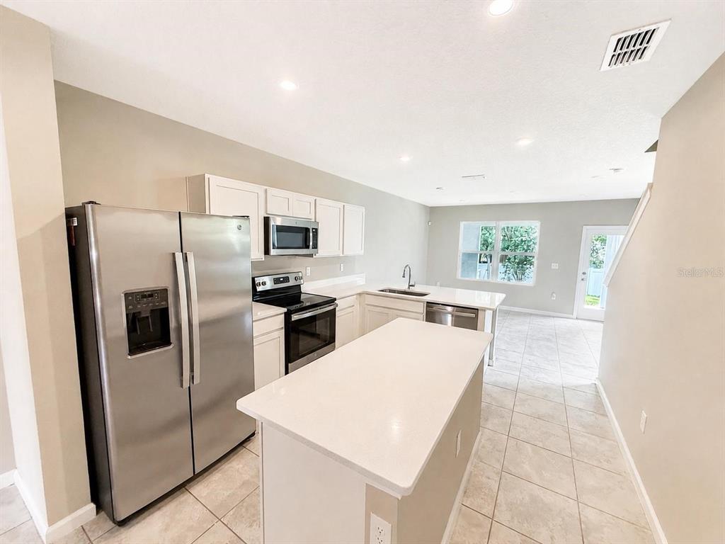 A kitchen features a stainless steel refrigerator, white cabinets, an island, and tile flooring — 2008 EDISON POINTE BOULEVARD, SOUTH DAYTONA, FL