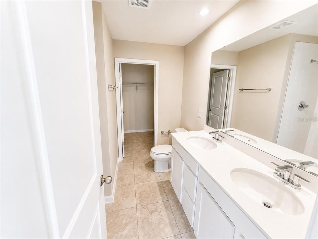 A bathroom features a double vanity with white cabinets, a toilet, and a walk-in closet — 2008 EDISON POINTE BOULEVARD, SOUTH DAYTONA, FL