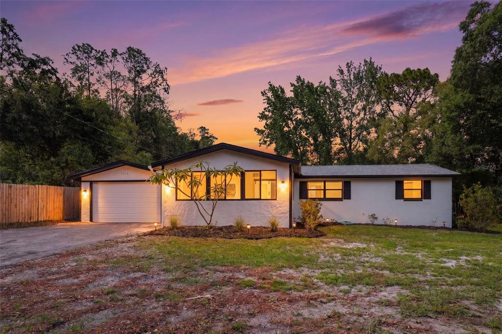 A single-story white house with a garage and a sunset sky in the background — 7229 PLATHE ROAD, NEW PORT RICHEY, FL