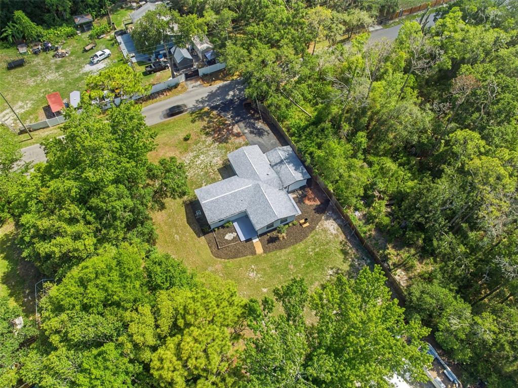 An aerial view shows a single-story house with a gray roof surrounded by dense trees — 7229 PLATHE ROAD, NEW PORT RICHEY, FL