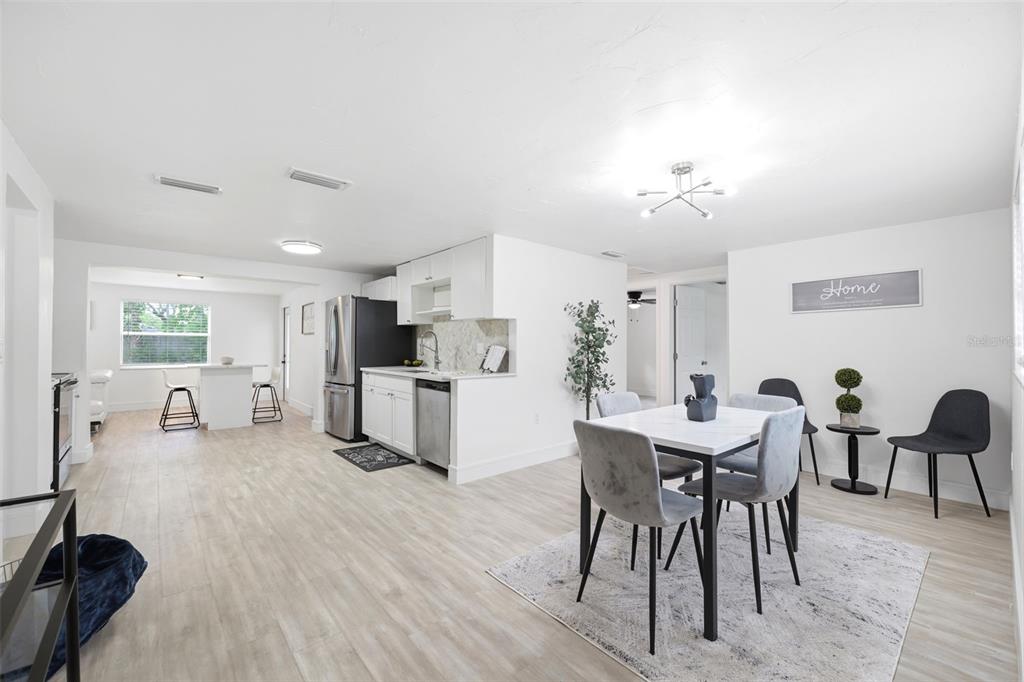 A bright, open-concept kitchen and dining area features white cabinetry, light wood-look flooring, and furniture — 7229 PLATHE ROAD, NEW PORT RICHEY, FL