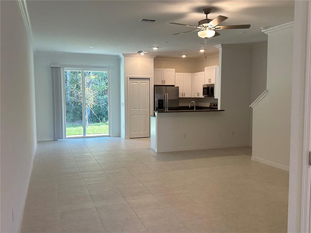 An open-concept living area features tile flooring, a kitchen with white cabinets, and sliding doors — 17437 NECTAR FLUME DRIVE, LAND O LAKES, FL