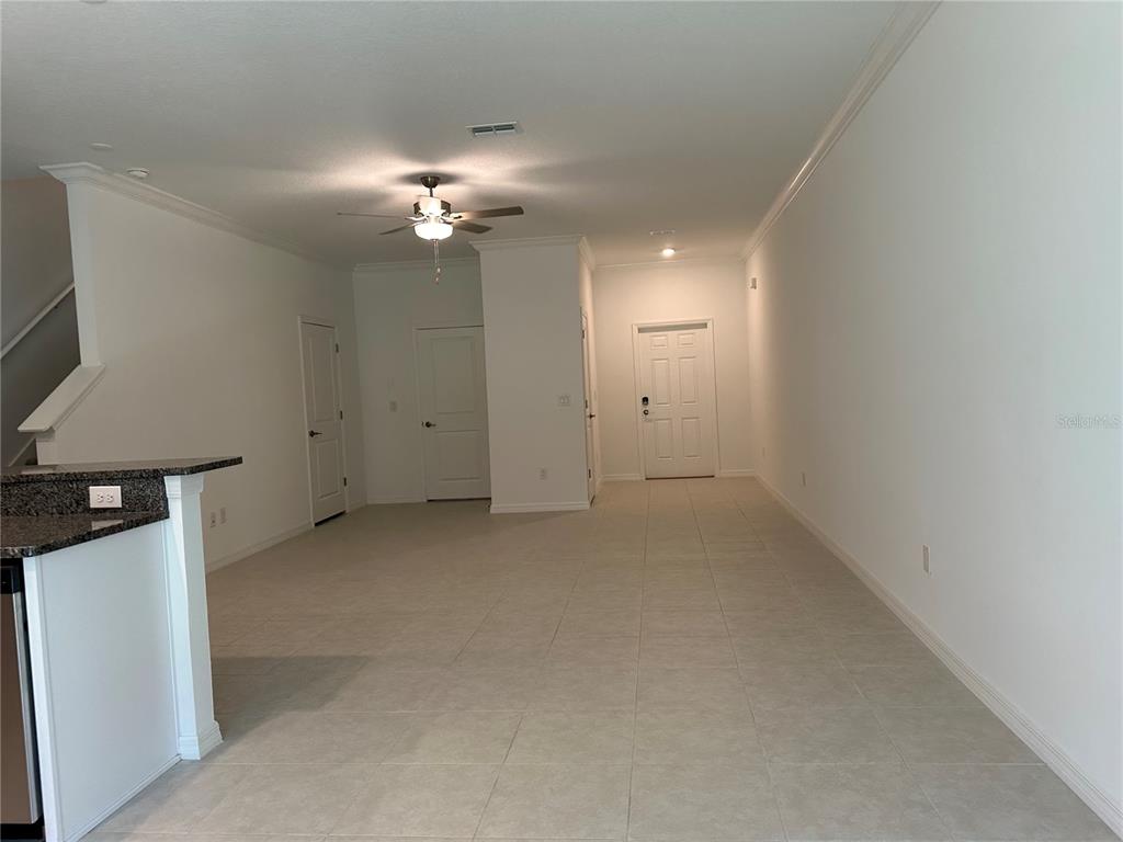 An open-concept living area features light tile flooring, white walls, a ceiling fan, and multiple doors — 17437 NECTAR FLUME DRIVE, LAND O LAKES, FL