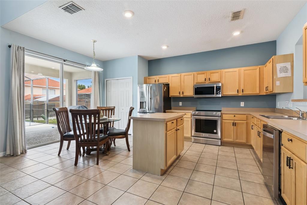 A kitchen with light wood cabinets, stainless steel appliances, a center island, and tile flooring — 143 CORDOVA AVENUE, DAVENPORT, FL