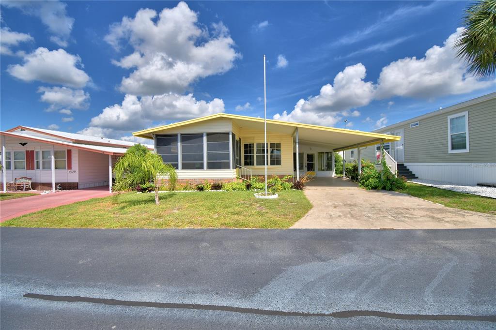 A yellow manufactured home with a screened porch and a carport sits on a lot — 4127 SPRUCEWOOD STREET, WINTER HAVEN, FL