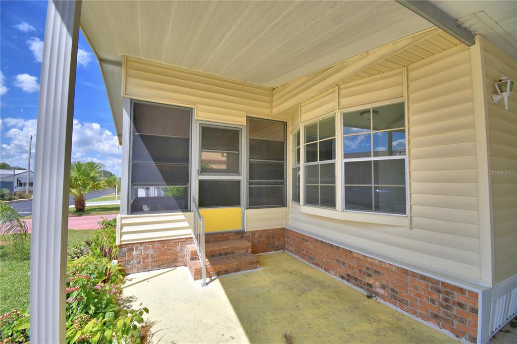 A covered porch with brick accents, a screen door, and light yellow siding — 4127 SPRUCEWOOD STREET, WINTER HAVEN, FL