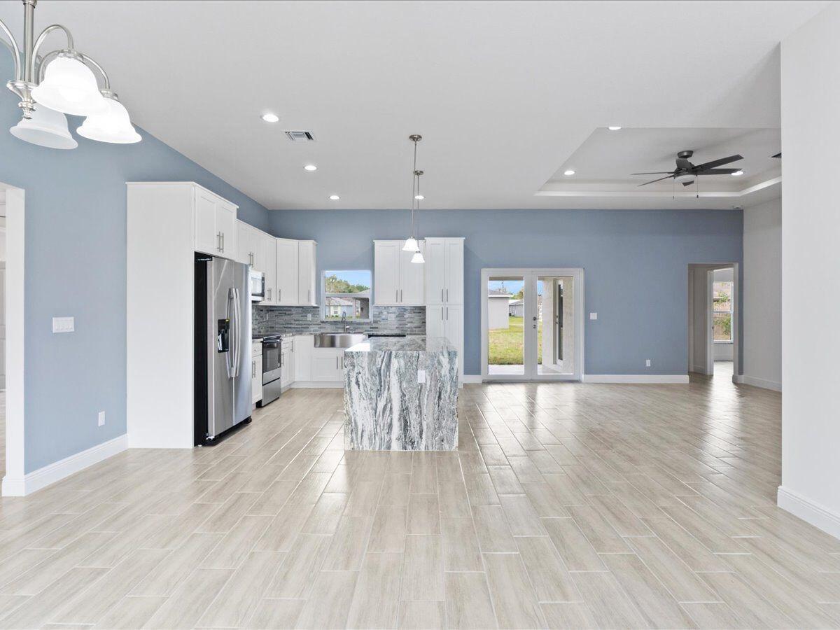 A modern kitchen features white cabinets, stone countertops, stainless steel appliances, and white marble flooring — 471 Saul Road SW, Palm Bay FL 32908, PALM BAY, FL