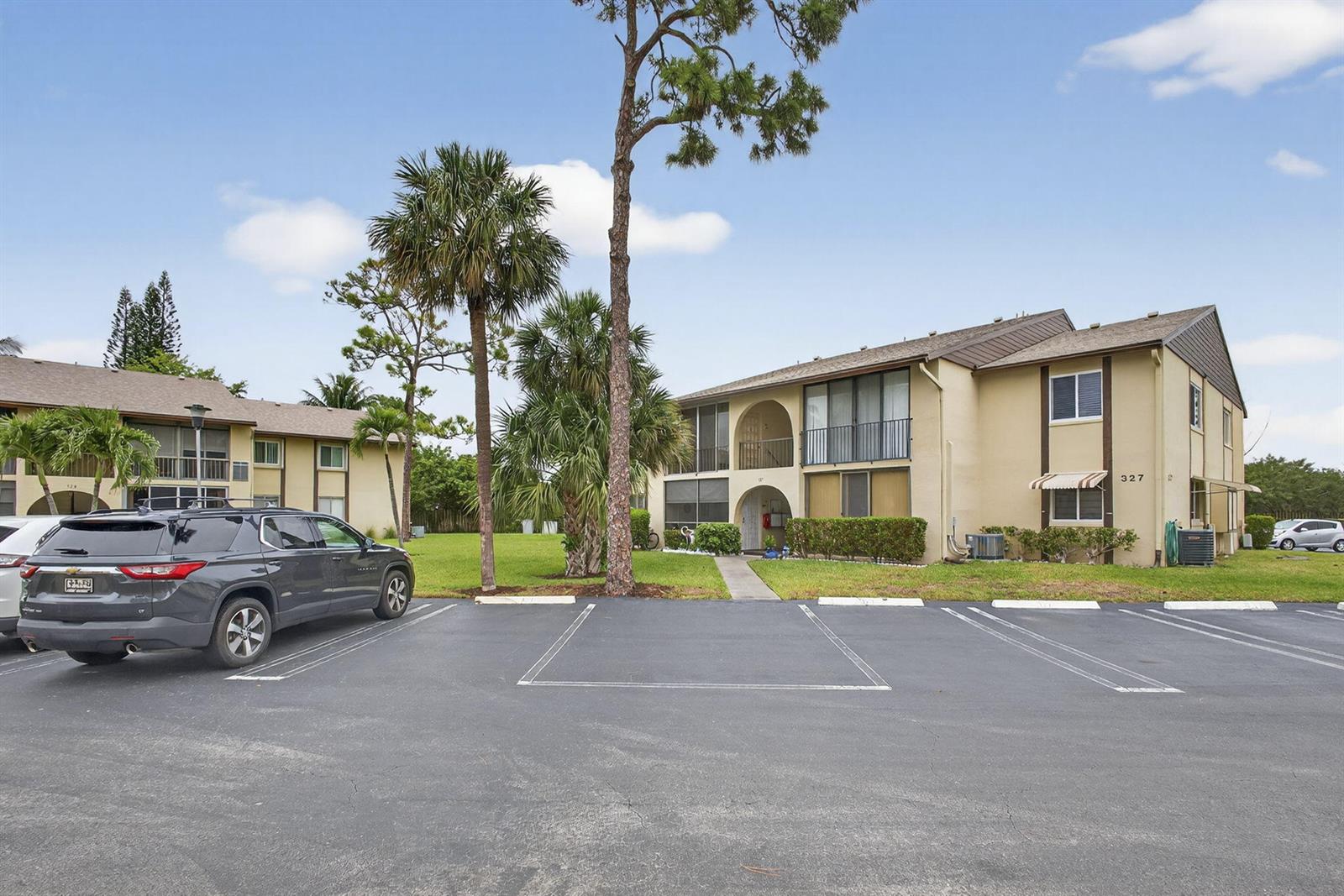 A two-story apartment building with a parking lot in the foreground and palm trees — 327 Pine Ridge Circle # 1, FL 33463, FL