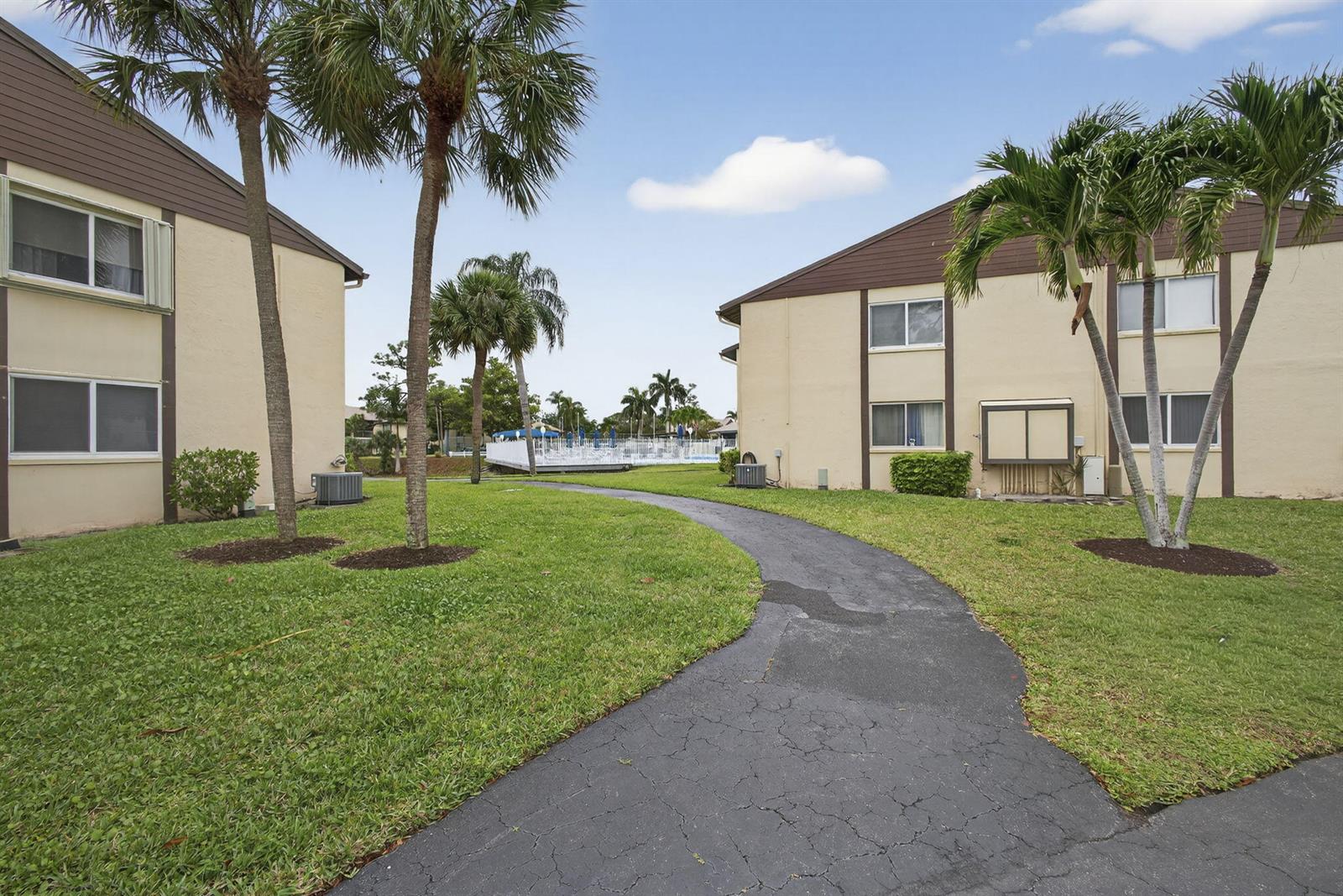 A paved walkway leads between two apartment buildings toward a swimming pool area — 327 Pine Ridge Circle # 1, FL 33463, FL