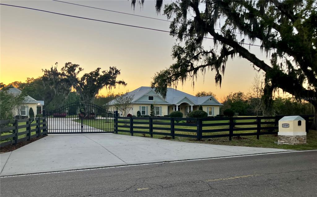 A yellow house with a metal roof sits behind a black fence and gated driveway — 3709 GALLAGHER ROAD, PLANT CITY, FL