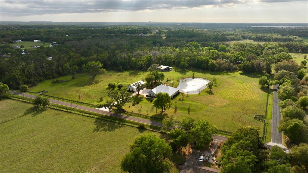 An aerial view of a rural property featuring a house, pond, and surrounding green pastures — 3709 GALLAGHER ROAD, PLANT CITY, FL