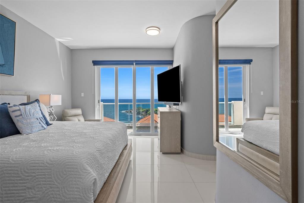 A bedroom features a bed, a television, and a large mirror overlooking the ocean — 1 SHELL CASTLE CLUB UNIT 74, HUMACAO, PR