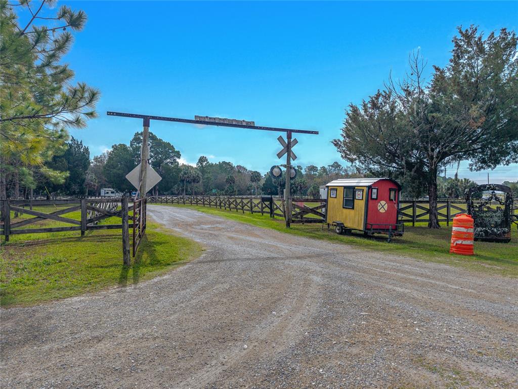 A gravel driveway leads through a gated entrance featuring a decorative railroad crossing sign — 11350 STATE ROAD 121, INGLIS, FL