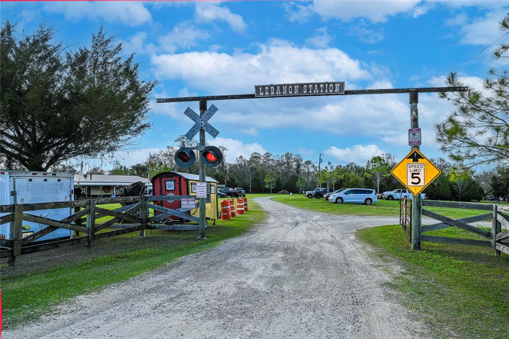 A gravel driveway leads through a railroad-themed entrance gate labeled Lebanon Station — 11350 STATE ROAD 121, INGLIS, FL