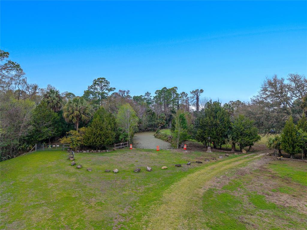 An aerial view shows a grassy yard leading to a small pond surrounded by trees — 11350 STATE ROAD 121, INGLIS, FL