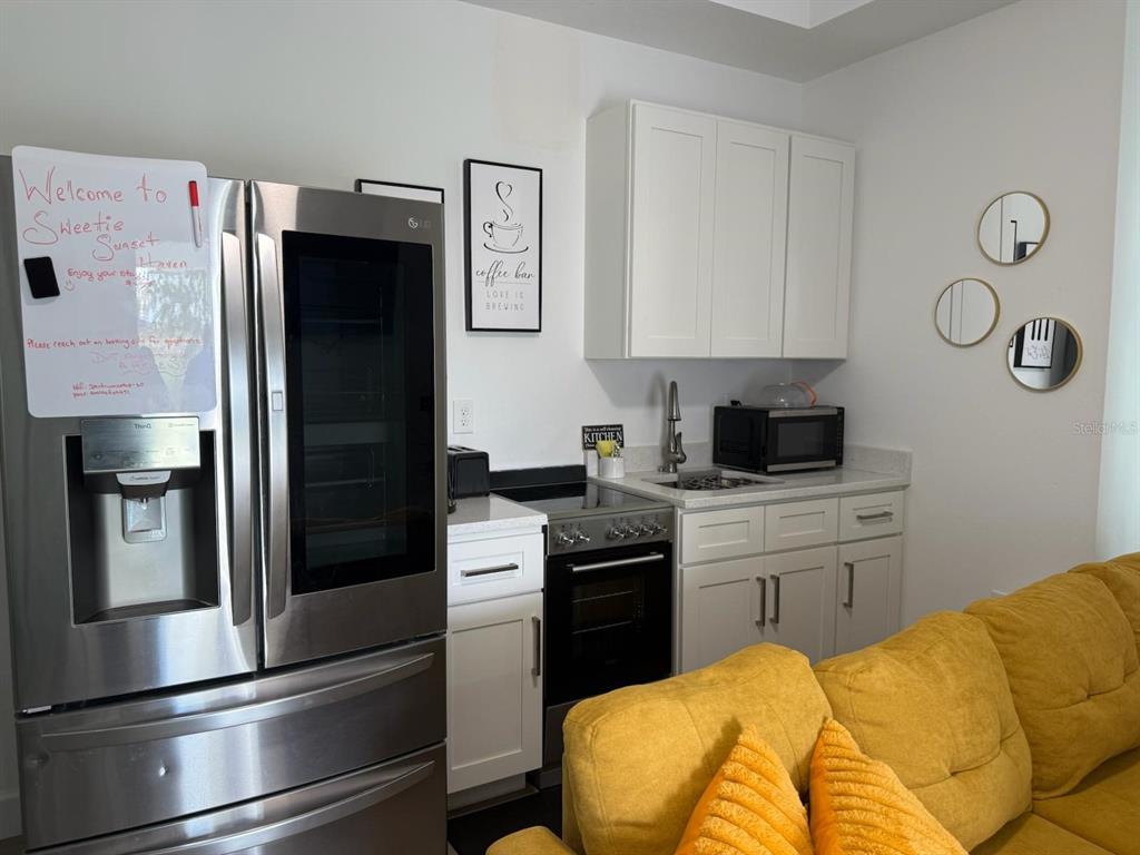A small kitchen features white cabinets, stainless steel appliances, and a yellow sofa in front — 2050 FLORIDA DEVELOPMENT ROAD UNIT A, DAVENPORT, FL