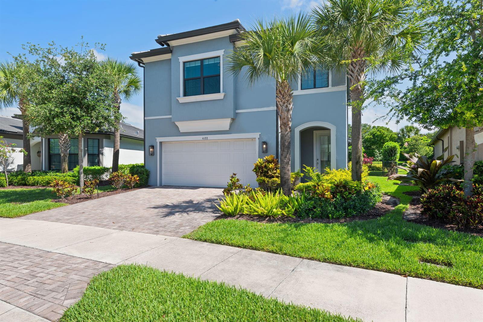 A two-story blue house features a white garage door, a paved driveway, and palm trees — 4688 E Pinehurst Trl Trail E, Oakland Park FL 33309, OAKLAND PARK, FL