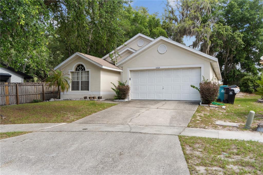 A single-story house with a white garage door, beige stucco exterior, and a concrete driveway — 5165 INNESBROOK COURT, ORLANDO, FL