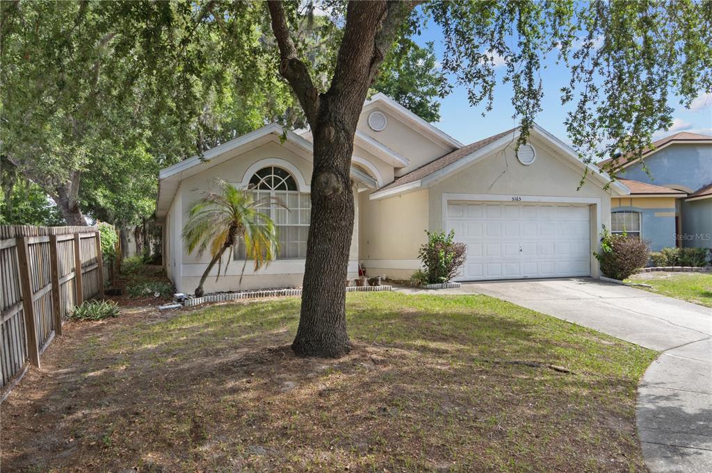 A single-story house with a beige stucco exterior, a two-car garage, and a large tree — 5165 INNESBROOK COURT, ORLANDO, FL