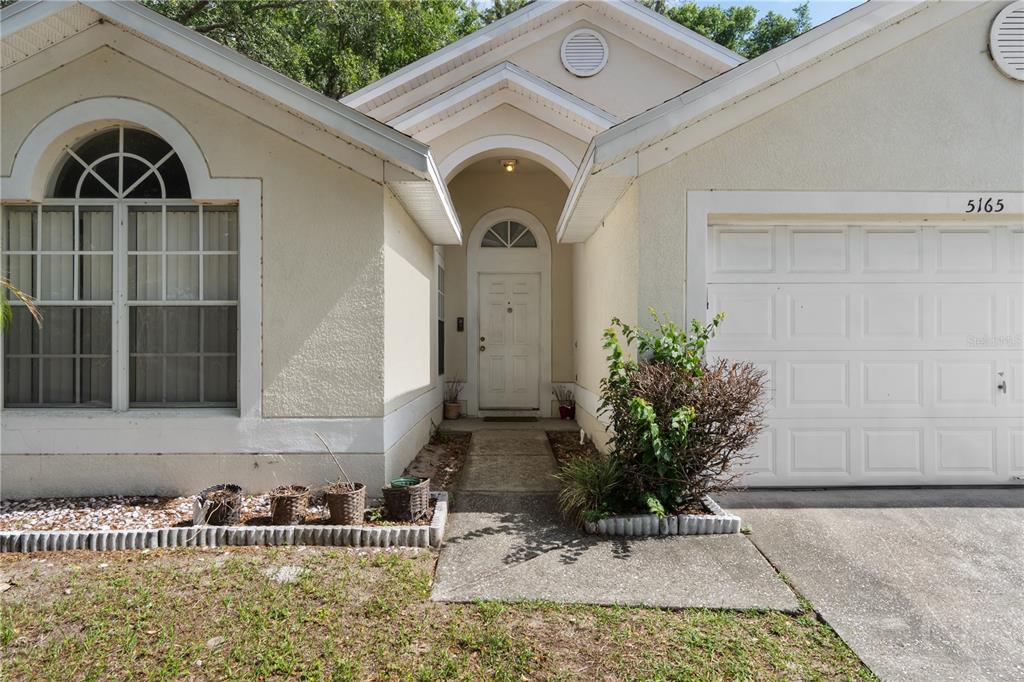 The exterior of a single-story house features a white garage, arched entryway, and front window — 5165 INNESBROOK COURT, ORLANDO, FL