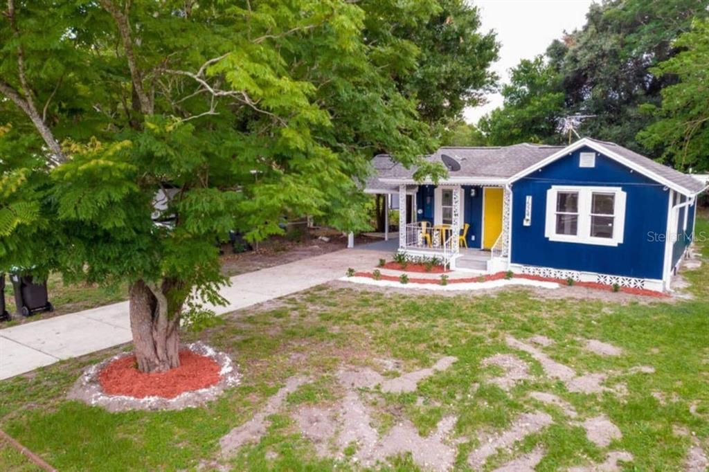 A blue single-story house with a yellow front door and a large tree in front — 7524 MARIETTA STREET, ORLANDO, FL
